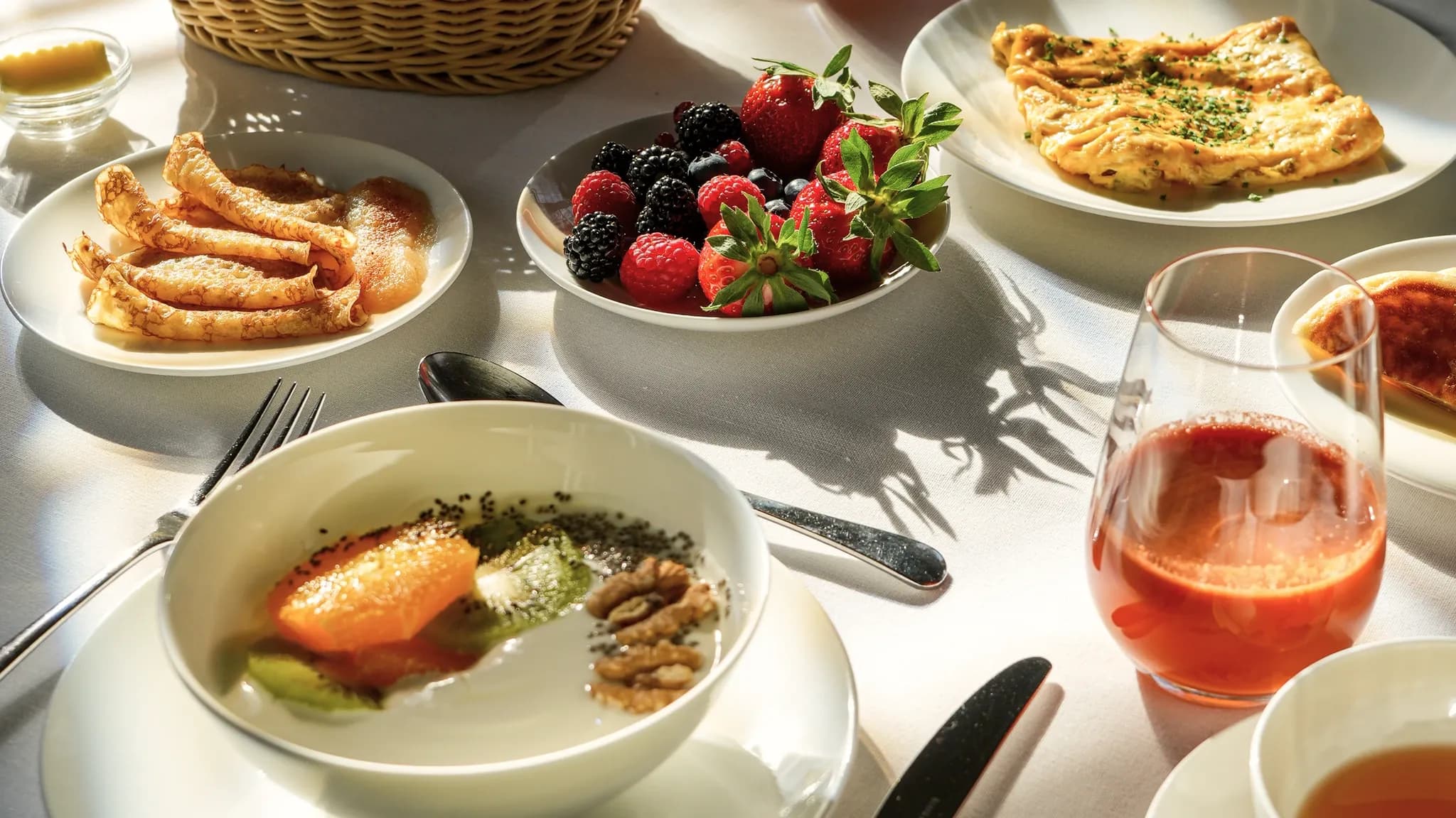 Blick von oben auf einen gedeckten Frühstückstisch mit Brotkorb, Beeren, Omelette, Crêpes und einem Aperitif.