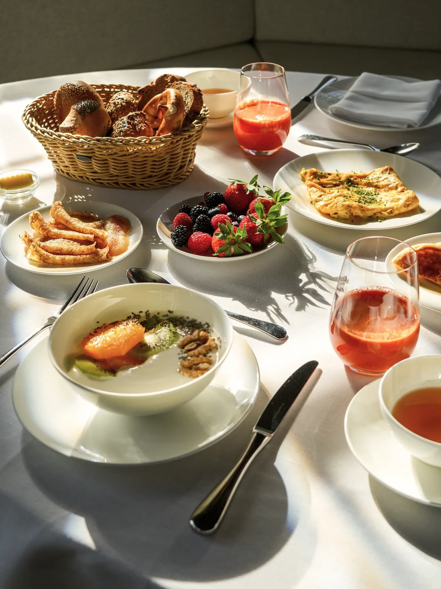 Blick von oben auf einen gedeckten Frühstückstisch mit Brotkorb, Beeren, Omelette, Crêpes und einem Aperitif.