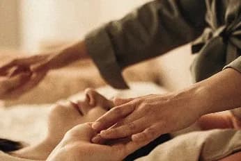 Kosmetische Behandlung: Hände einer Therapeutin an Kopf und Hand einer entspannt liegenden Person