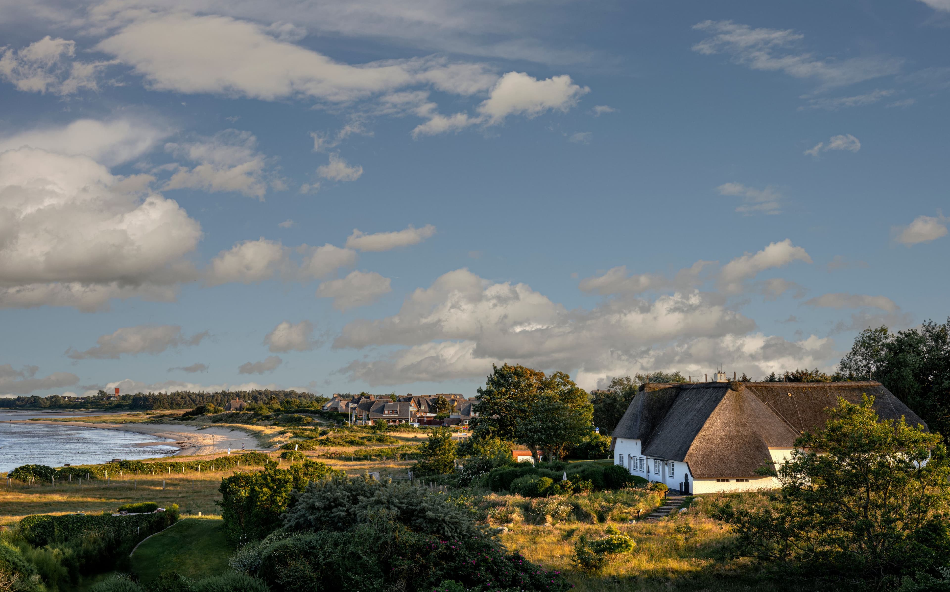 Friesisches Reetdachhaus in der Dünenlandschaft von Sylt, links die Wattenmeerküste unter bewölktem Himmel