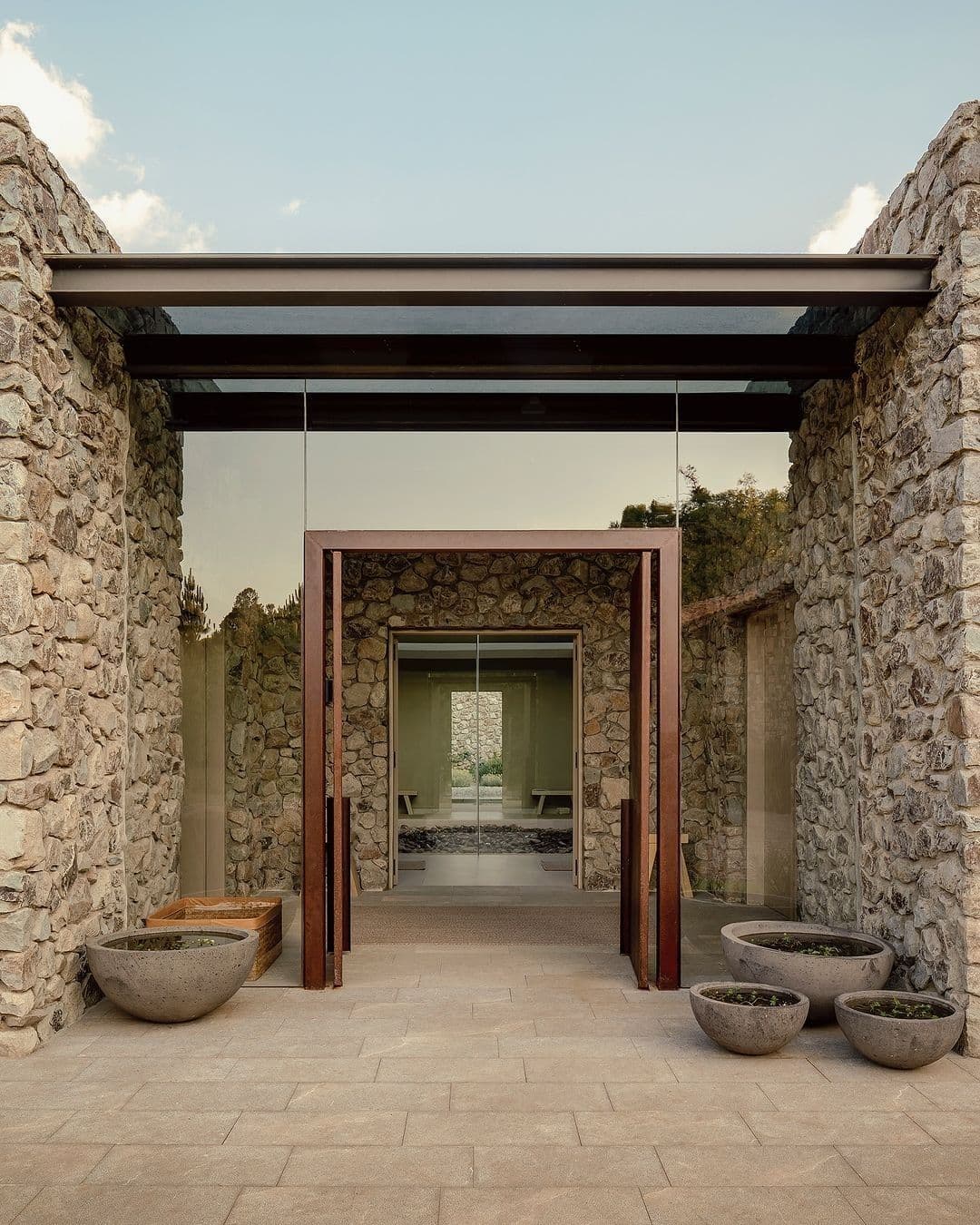 Architektonischer Spa-Innenhof mit Steinwänden, Cortenstahl-Türportalen, Glaswänden und runden Betonpflanzgefäßen