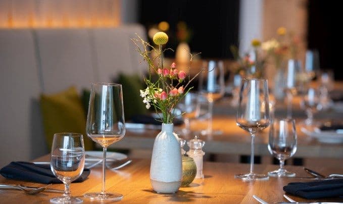 Eingedeckter Tisch mit mehreren Weingläsern, Stoffservietten und einer kleinen Blumenvase.