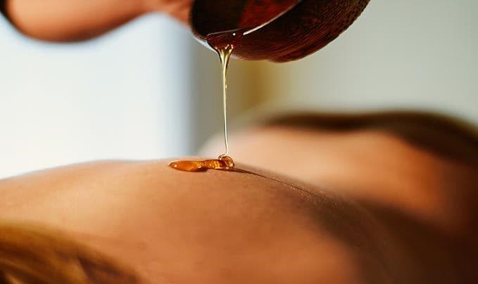 Treatment im Engel Obertal – warmes goldenes Öl wird während einer Behandlung sanft auf die Haut gegossen.