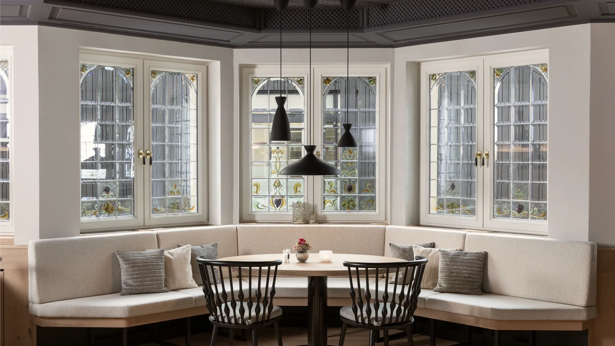 Erkerfenster mit gepolsterter Sitzbank, Tischen und schwarzen Pendelleuchten.