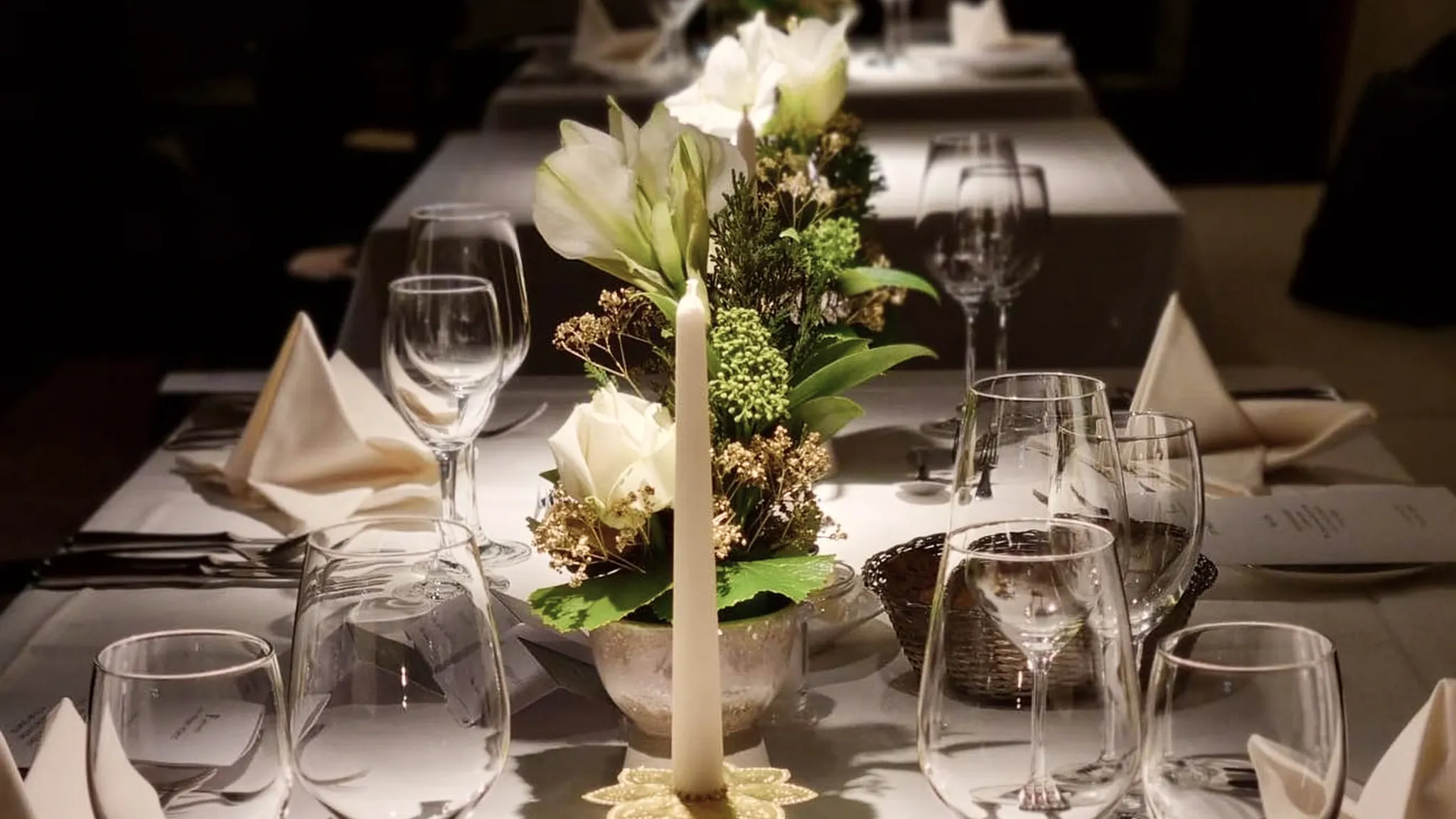 Lange festlich eingedeckte Tafel mit Kerzenleuchter, Blumenschmuck und Kristallgläsern.