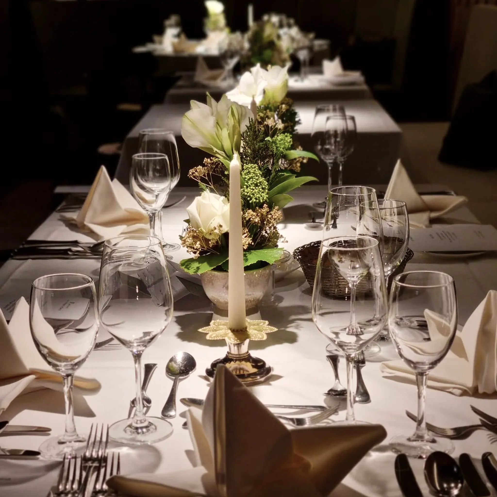 Lange festlich eingedeckte Tafel mit Kerzenleuchter, Blumenschmuck und Kristallgläsern.