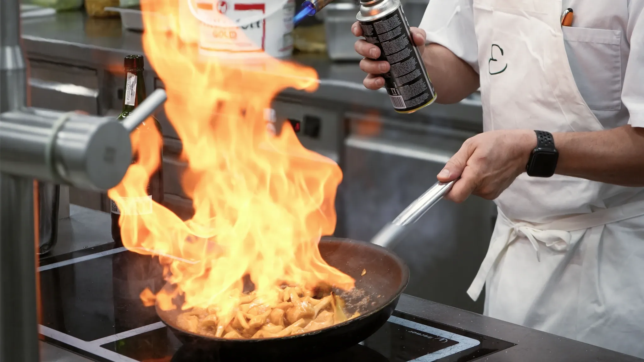 Koch flambiert in einer Pfanne, eine hohe Stichflamme schlägt auf.