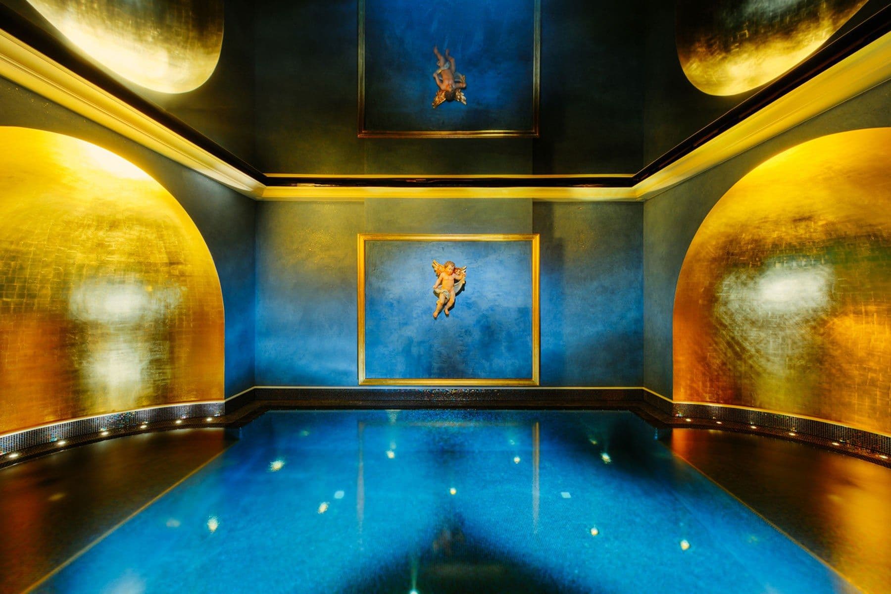 Blau beleuchteter Floating-Pool mit goldschimmernden Waenden, Engelsrelief und Gemaelde im Spa Wolke 7