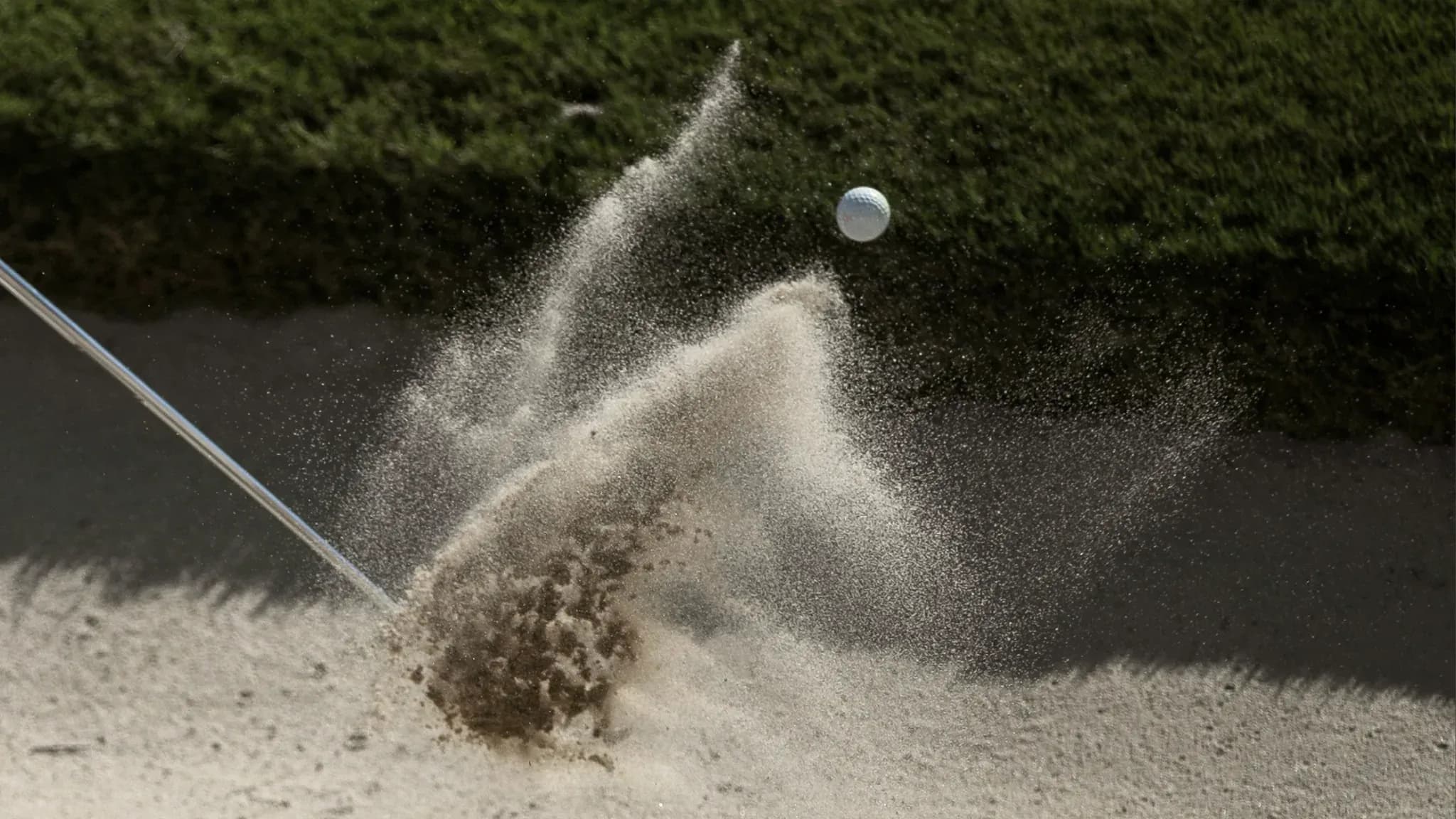 Golfball fliegt aus einem Sandbunker, aufgewirbelter Sand im Gegenlicht.
