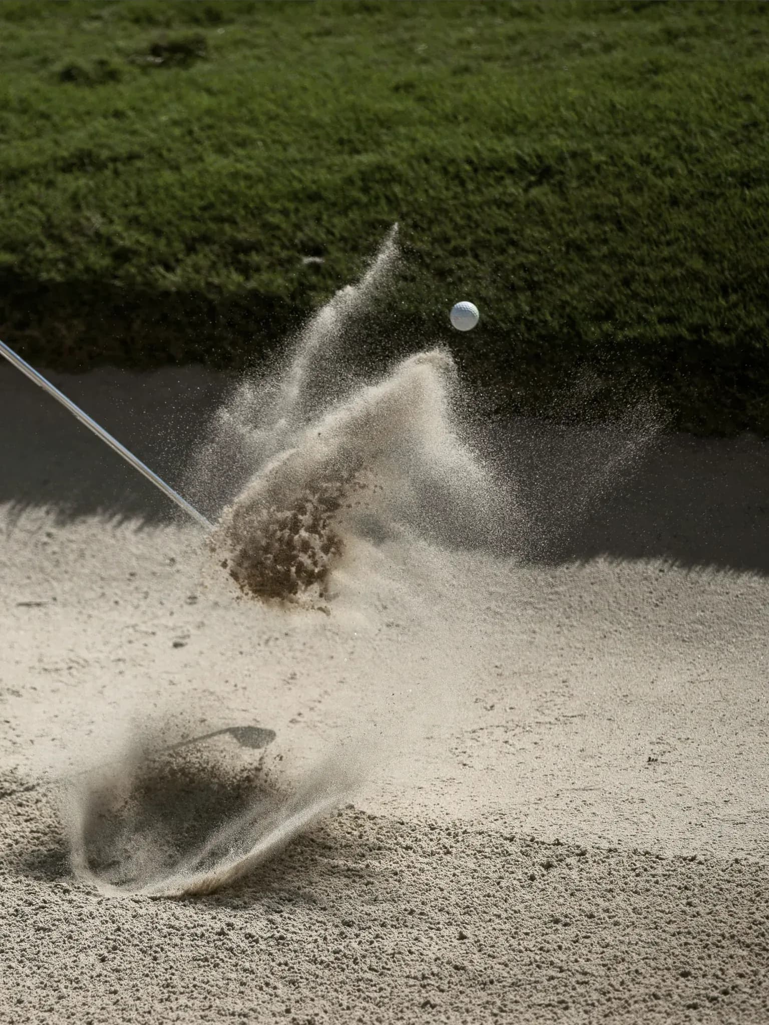 Golfball fliegt aus einem Sandbunker, aufgewirbelter Sand im Gegenlicht.
