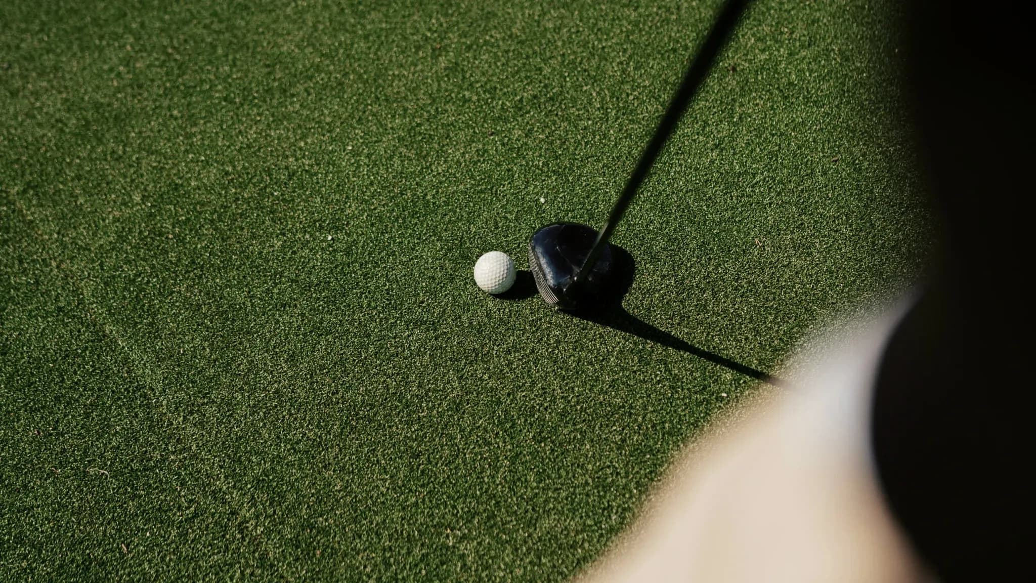 Golfball liegt neben einem Driver-Schlägerkopf auf kurz geschnittenem Rasen.