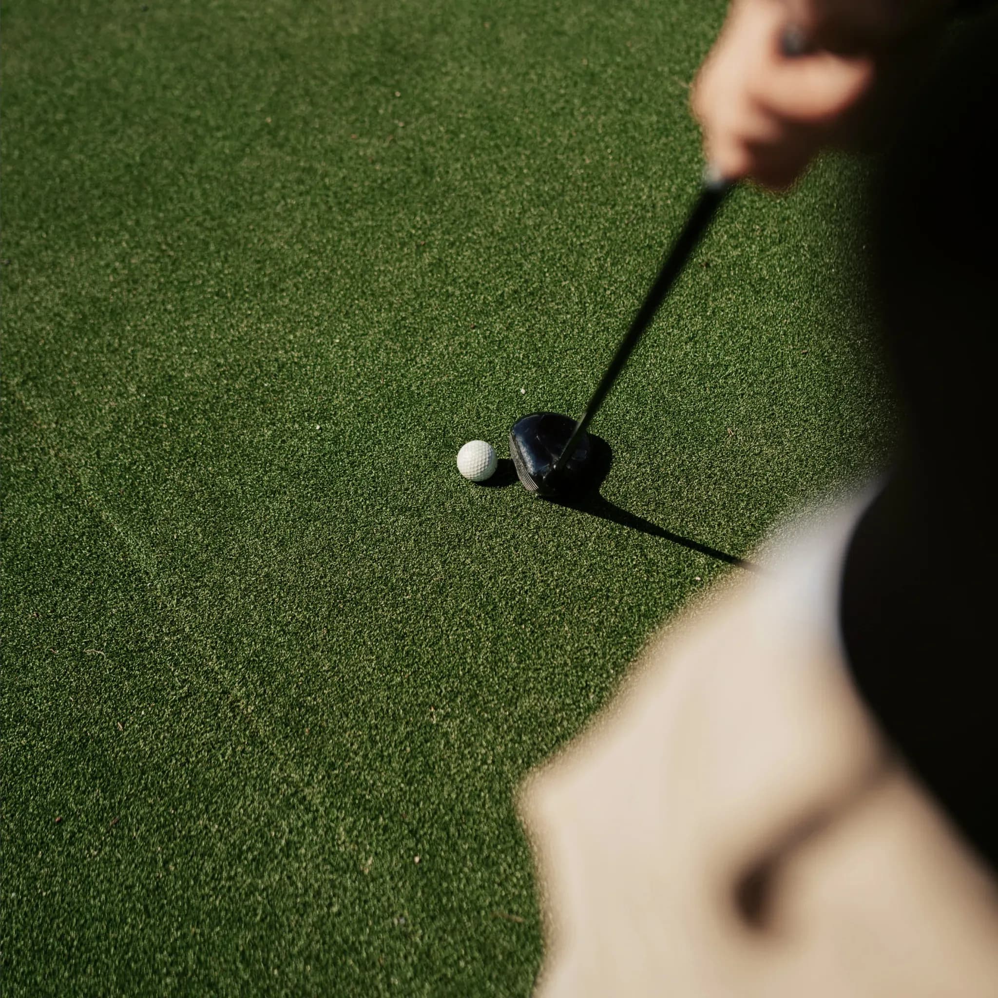 Golfball liegt neben einem Driver-Schlägerkopf auf kurz geschnittenem Rasen.