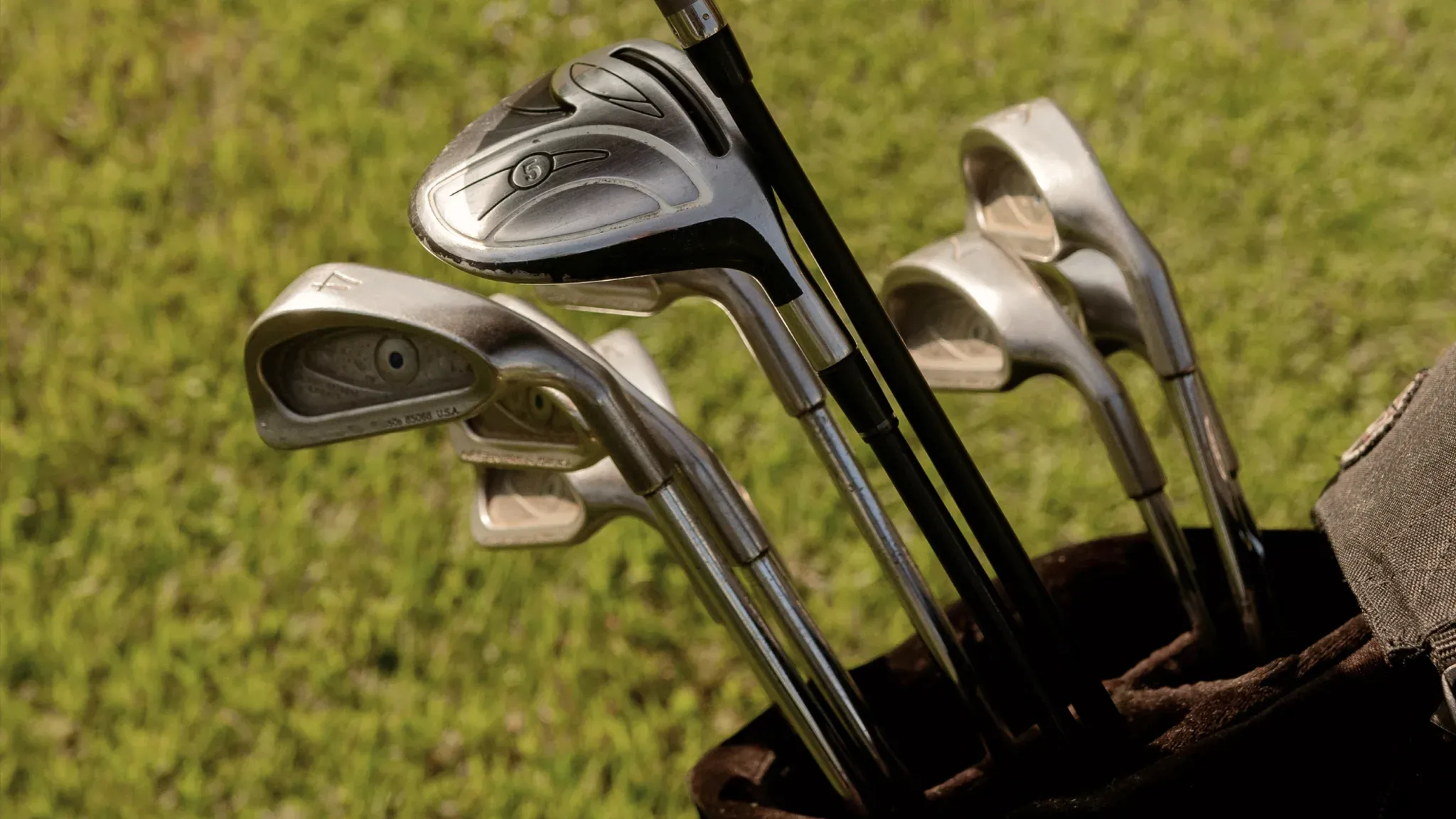 Mehrere Eisen stecken in einem Golfbag auf der Wiese.