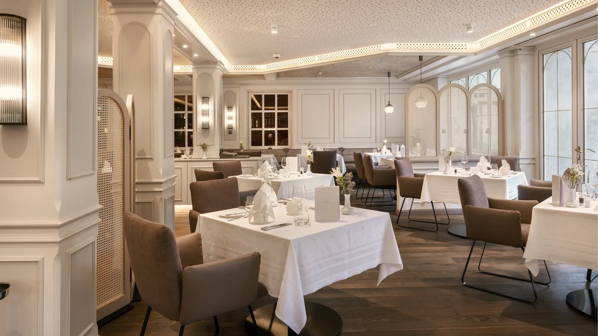 Klassischer Restaurantsaal mit weiß eingedeckten Tischen und hohen Sprossenfenstern.