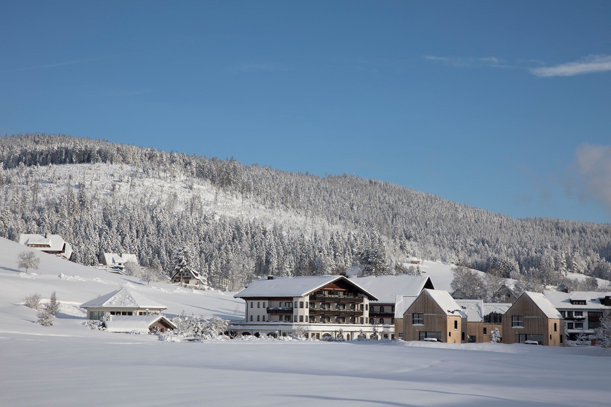 Das Engel Obertal mit seinen Chalets in tief verschneiter Winterlandschaft vor bewaldetem Hang unter blauem Himmel.