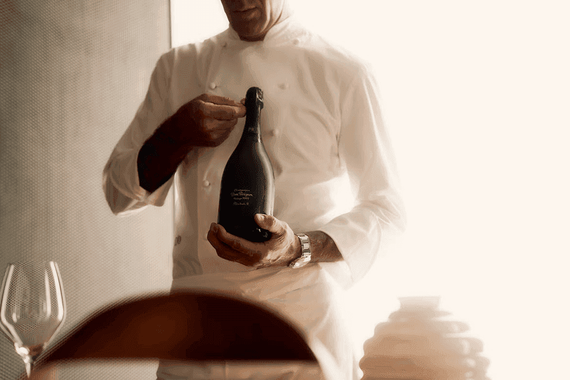 Sommelier in weißer Jacke hält eine Flasche Dom-Pérignon-Champagner im weichen Fensterlicht