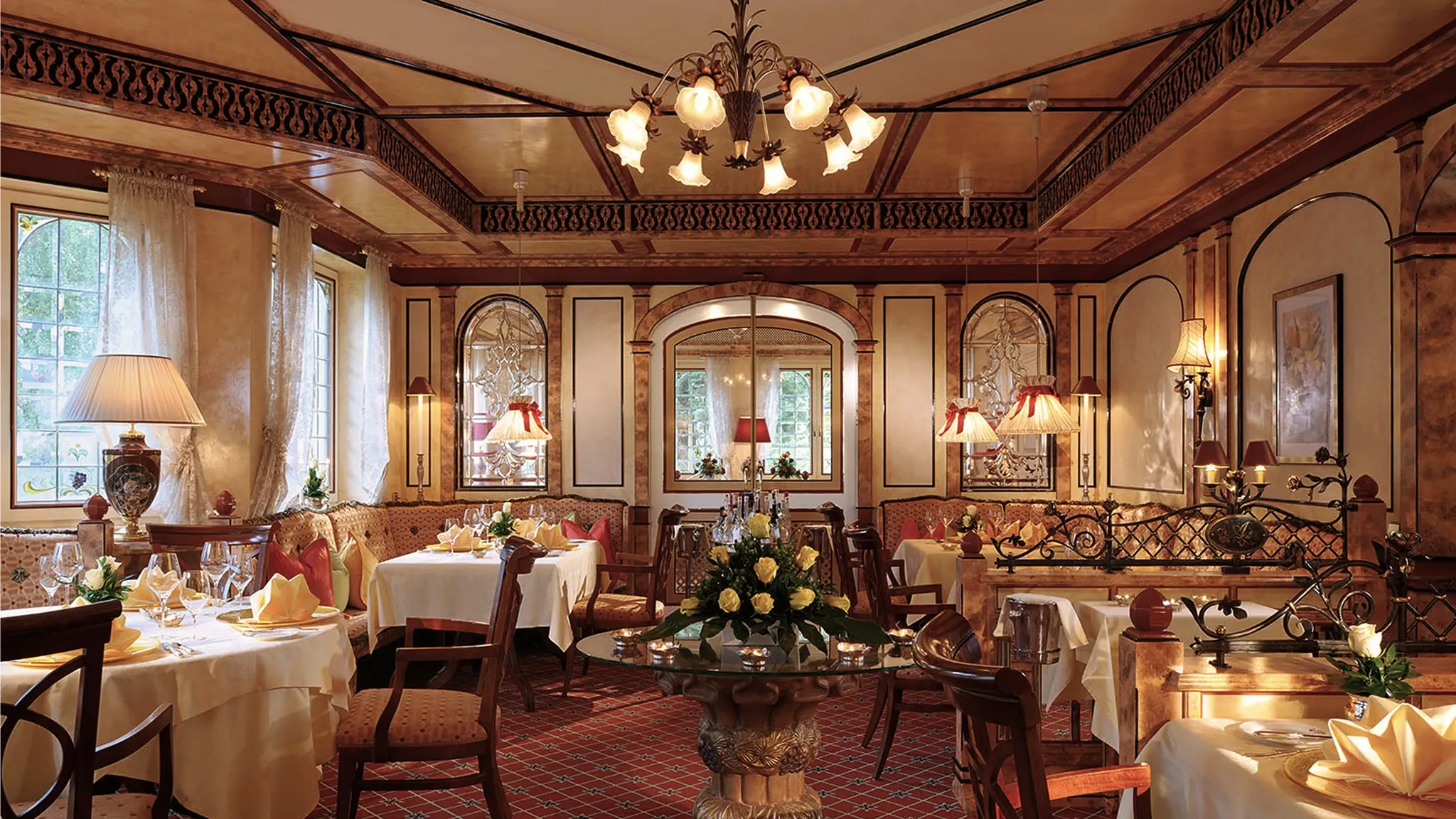 Restaurantsaal mit rotem Teppich, Kronleuchtern, Blumengesteck und weiß eingedeckten Tischen.