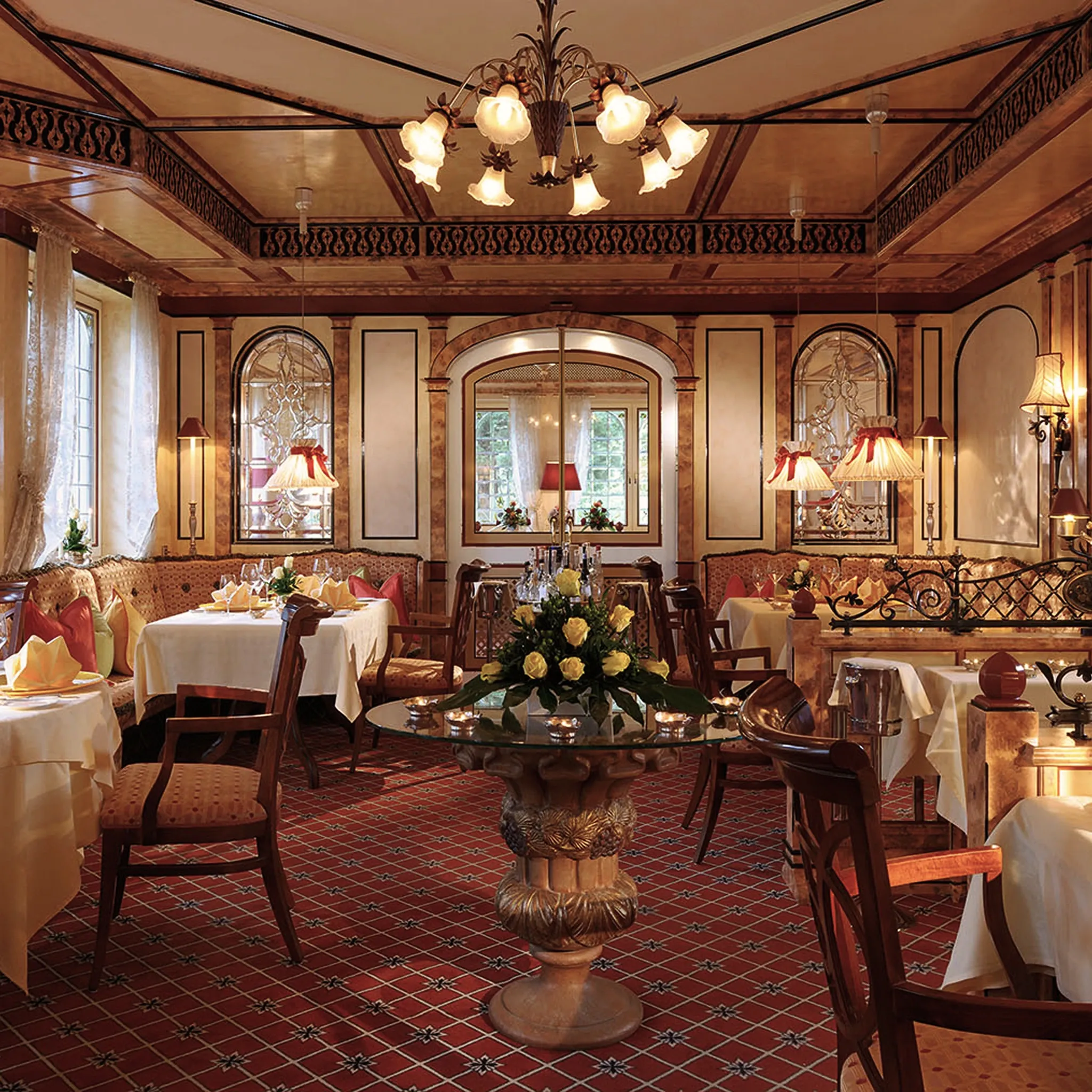 Restaurantsaal mit rotem Teppich, Kronleuchtern, Blumengesteck und weiß eingedeckten Tischen.