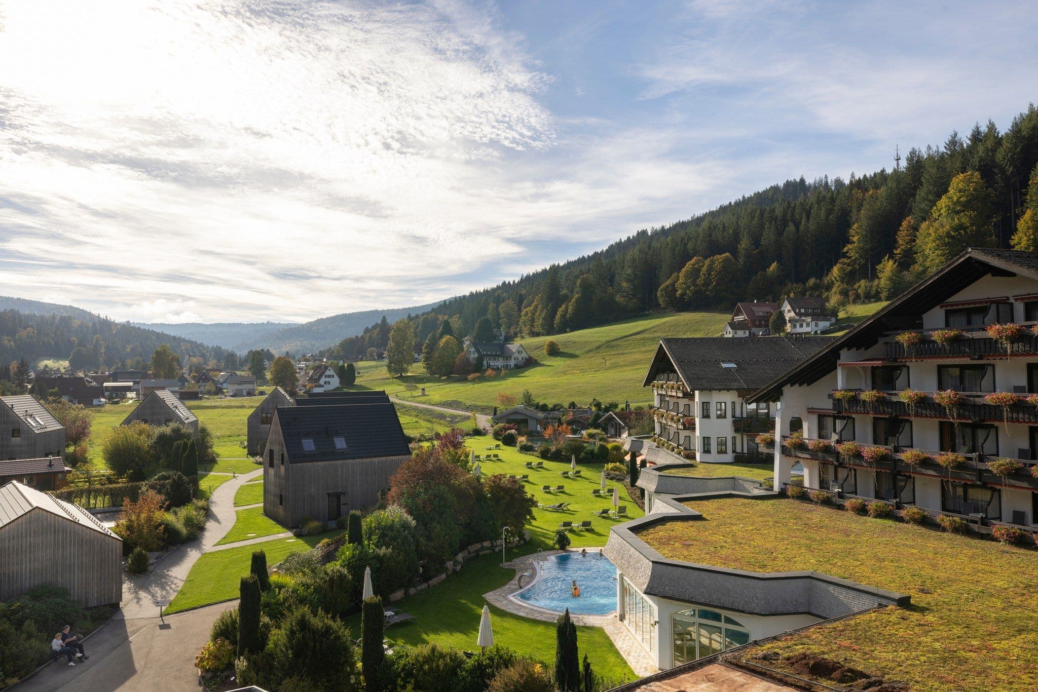 Luftaufnahme des Engel Obertal am Sommerabend: Hotelgebaeude und Chalets mit Aussenpool, dahinter bewaldete Schwarzwaldhuegel