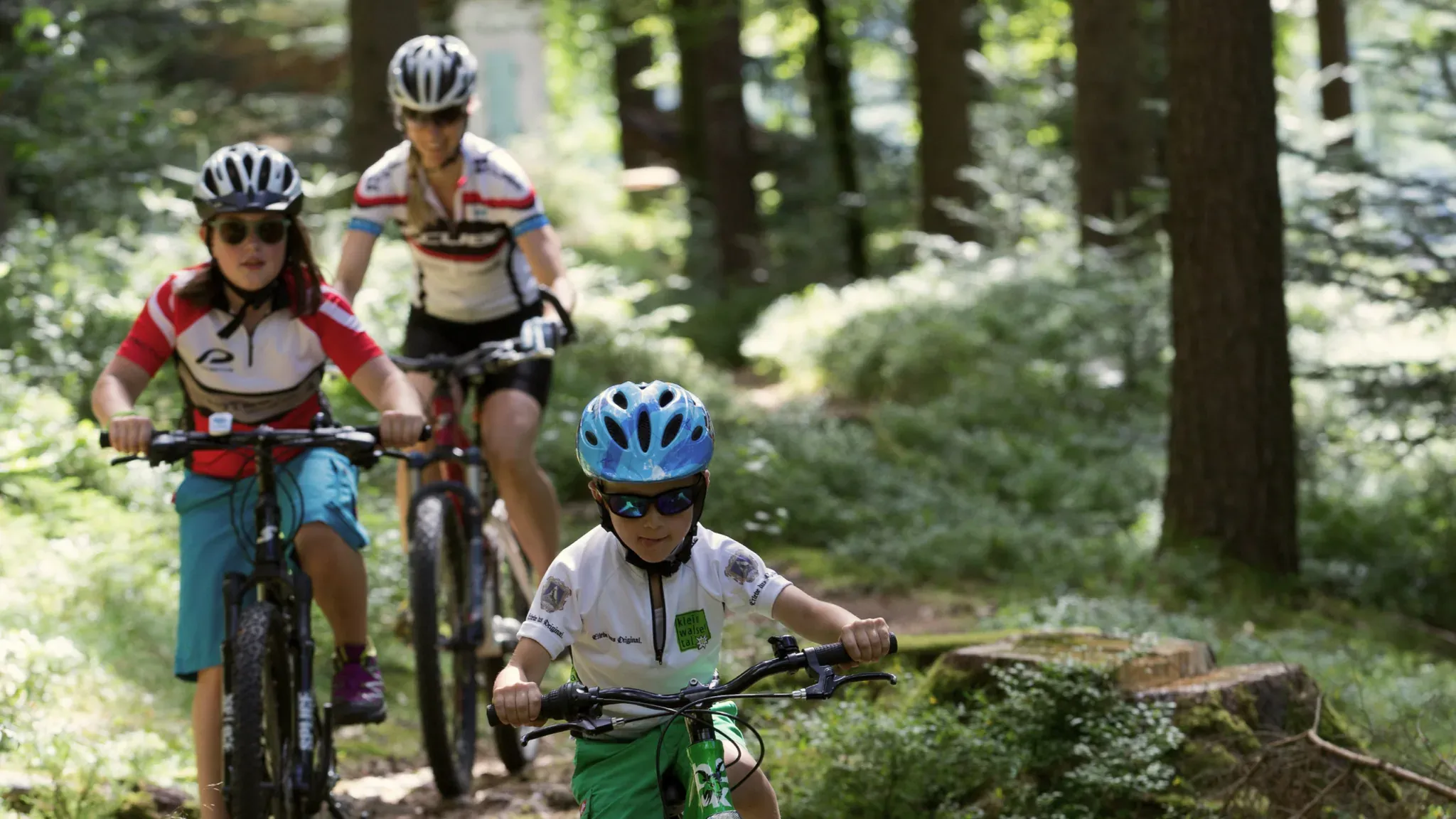 Zwei Kinder und eine Frau fahren mit Mountainbikes über einen Waldweg.