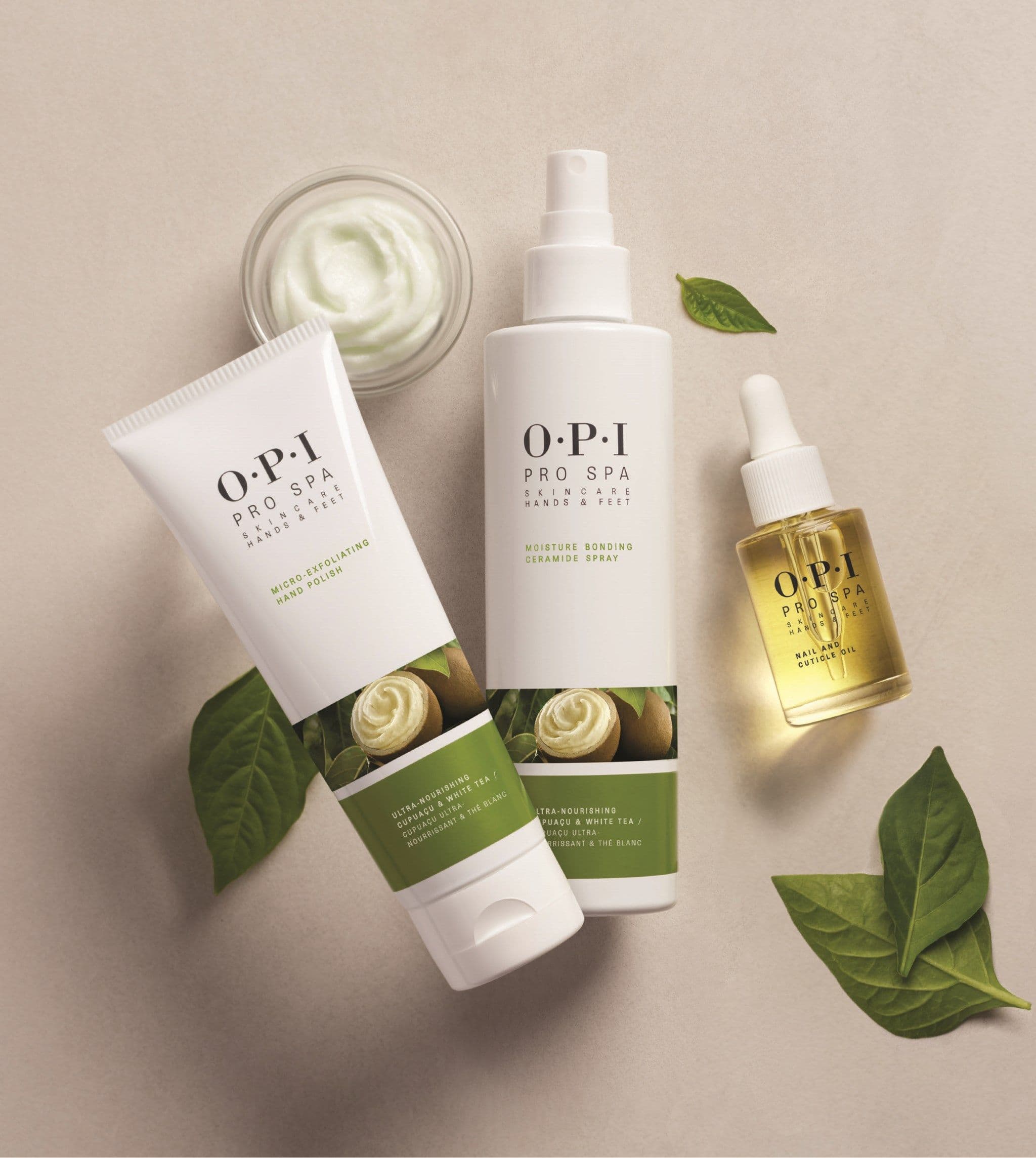 Micro-Exfoliating Hand Polish, Moisture Bonding Ceramide Spray und Nail and Cuticle Oil der Linie OPI Pro Spa auf hellem Untergrund, umgeben von grünen Blättern.