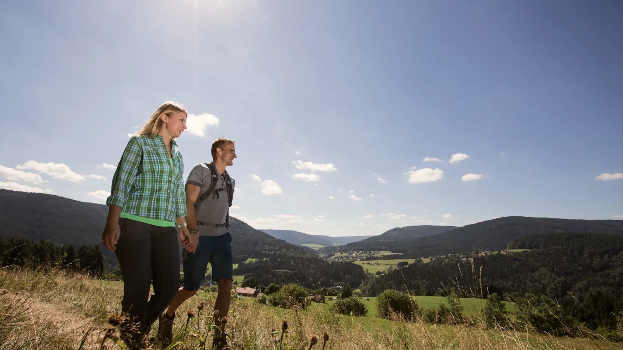Ein Paar wandert über eine Höhenwiese mit weitem Blick über die Schwarzwaldberge.