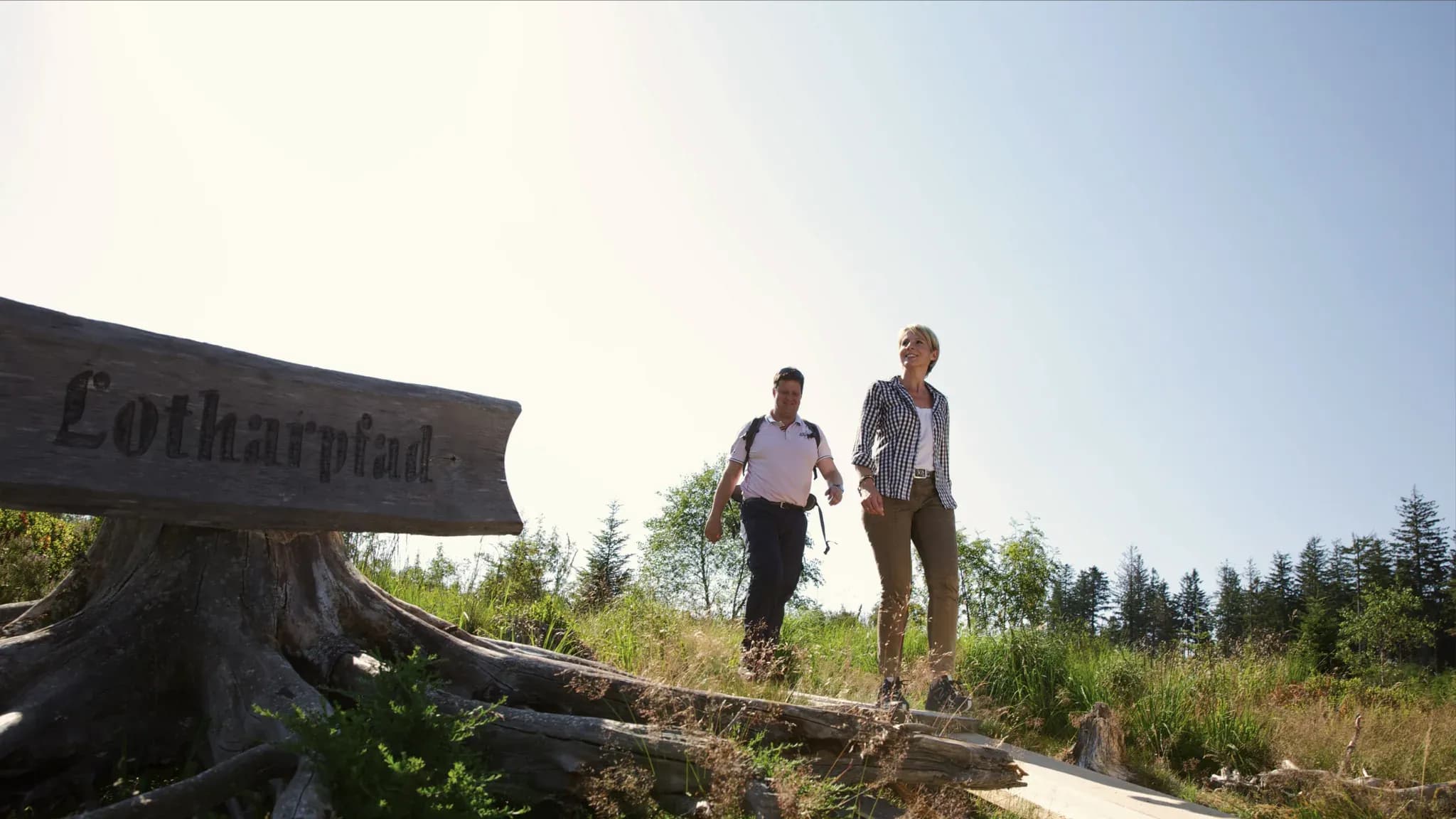 Hölzerner Wegweiser mit der Aufschrift Lotharpfad, dahinter zwei Wanderer auf dem Weg.