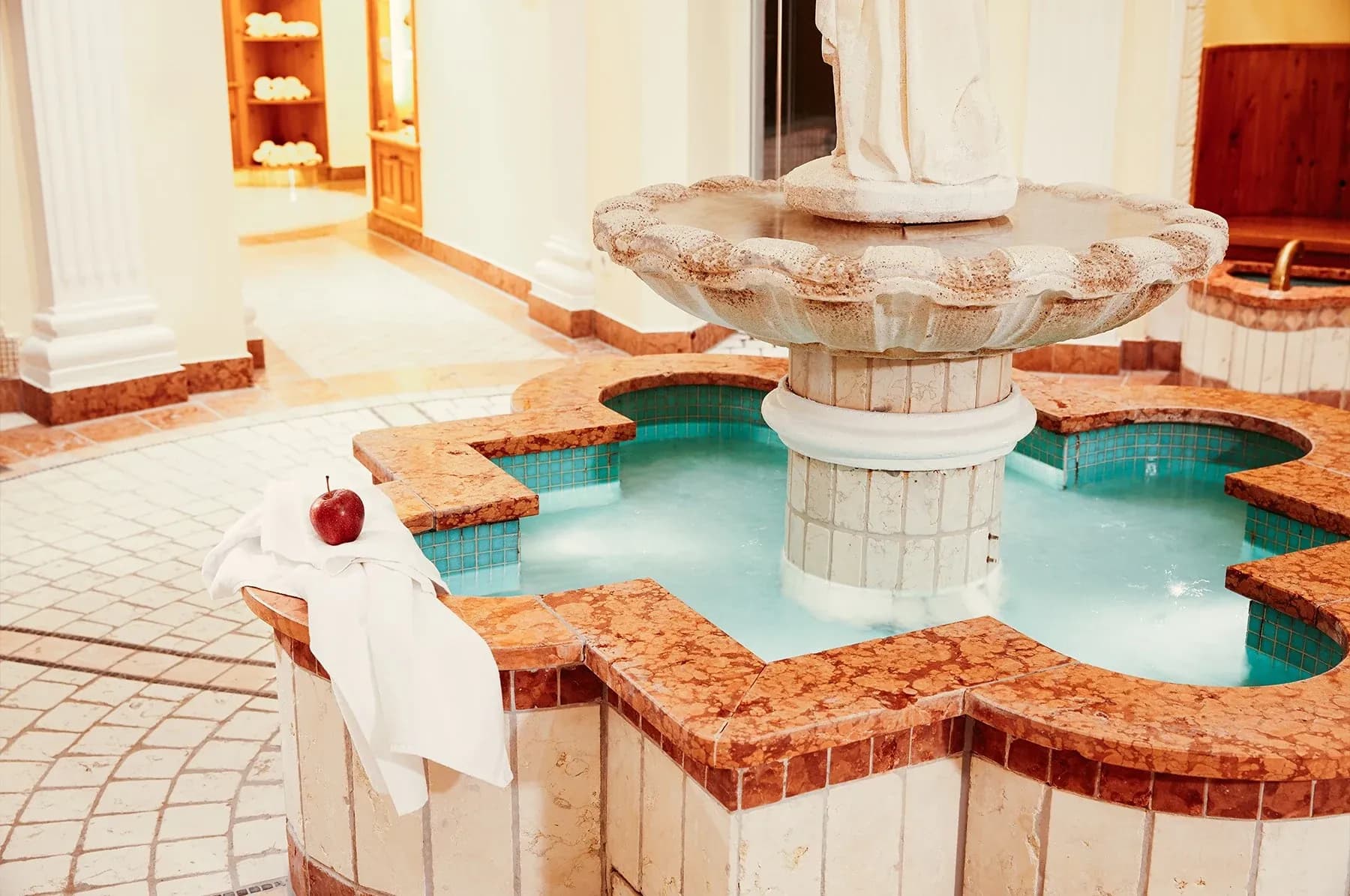 Whirlpool mit steinernem Springbrunnen und Säulen, ein Bademantel liegt über dem Beckenrand
