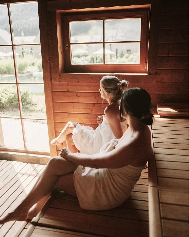 Zwei Frauen in Handtücher gehüllt sitzen in der Sauna am Panoramafenster