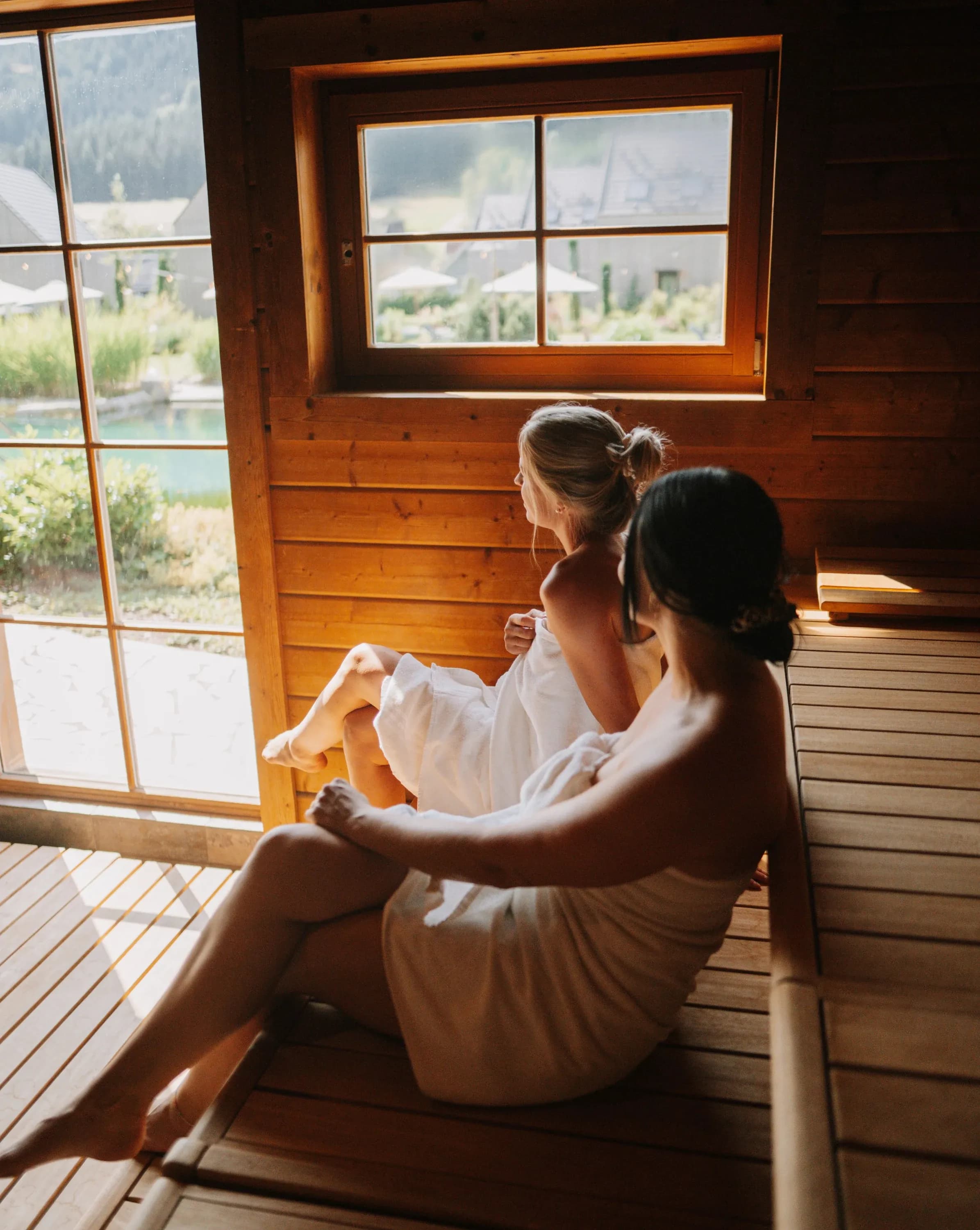 Zwei Frauen in Handtücher gehüllt sitzen in der Sauna am Panoramafenster