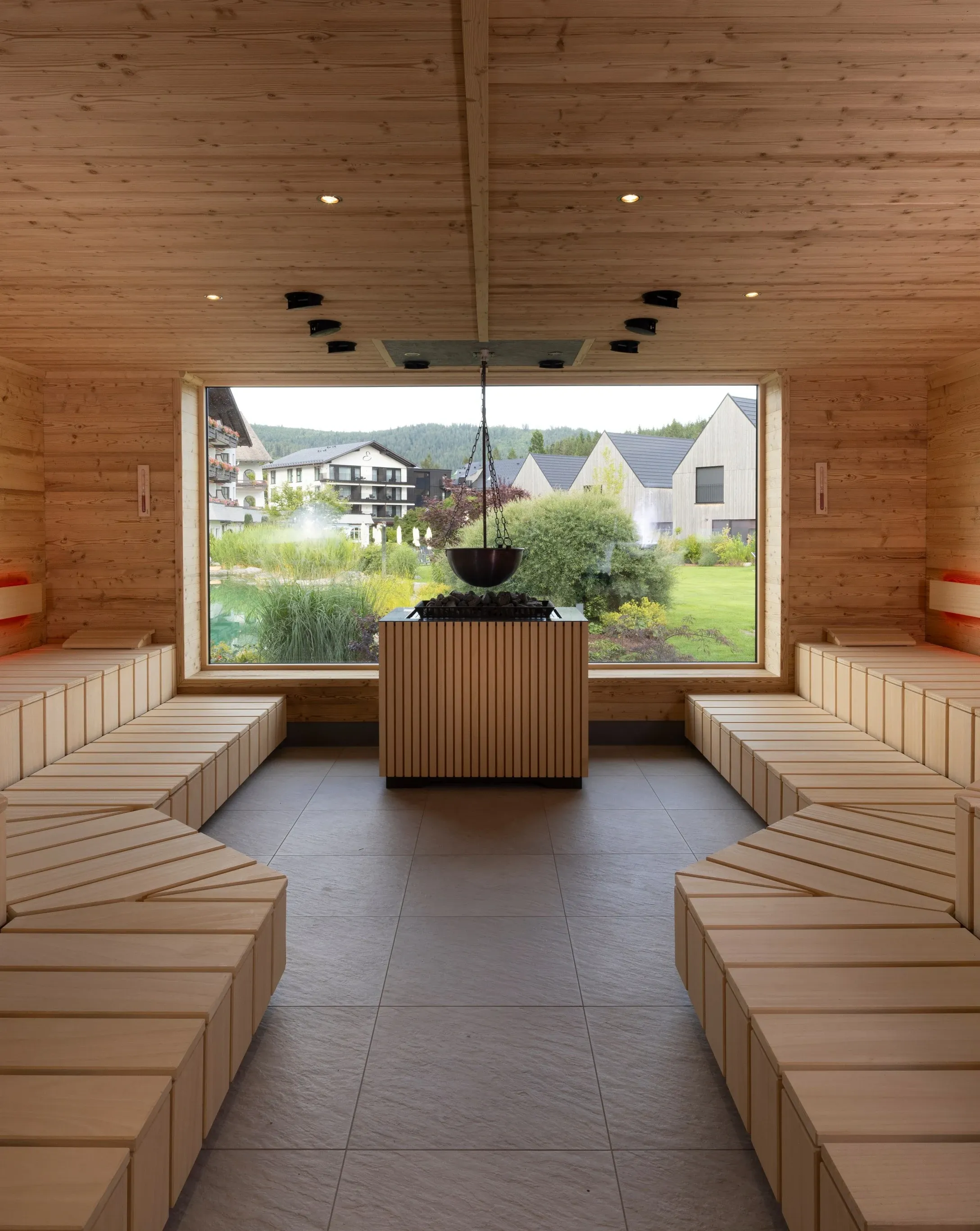 Helle Holzsauna mit großem Panoramafenster und Blick auf Wiesen und Häuser
