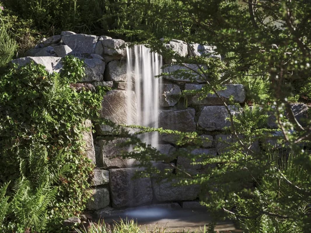 Wasserfall fällt über bemooste Felsen, umgeben von dichtem Grün