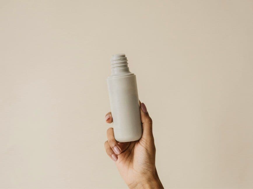 Hand hält eine schlichte weiße Pflegeflasche vor beigem Hintergrund