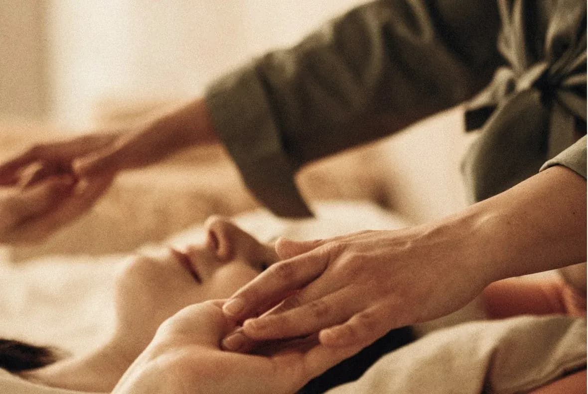 Kosmetische Behandlung: Hände einer Therapeutin an Kopf und Hand einer entspannt liegenden Person