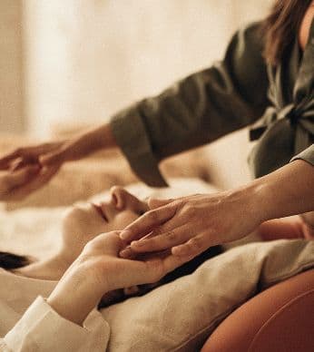Kosmetische Behandlung: Hände einer Therapeutin an Kopf und Hand einer entspannt liegenden Person