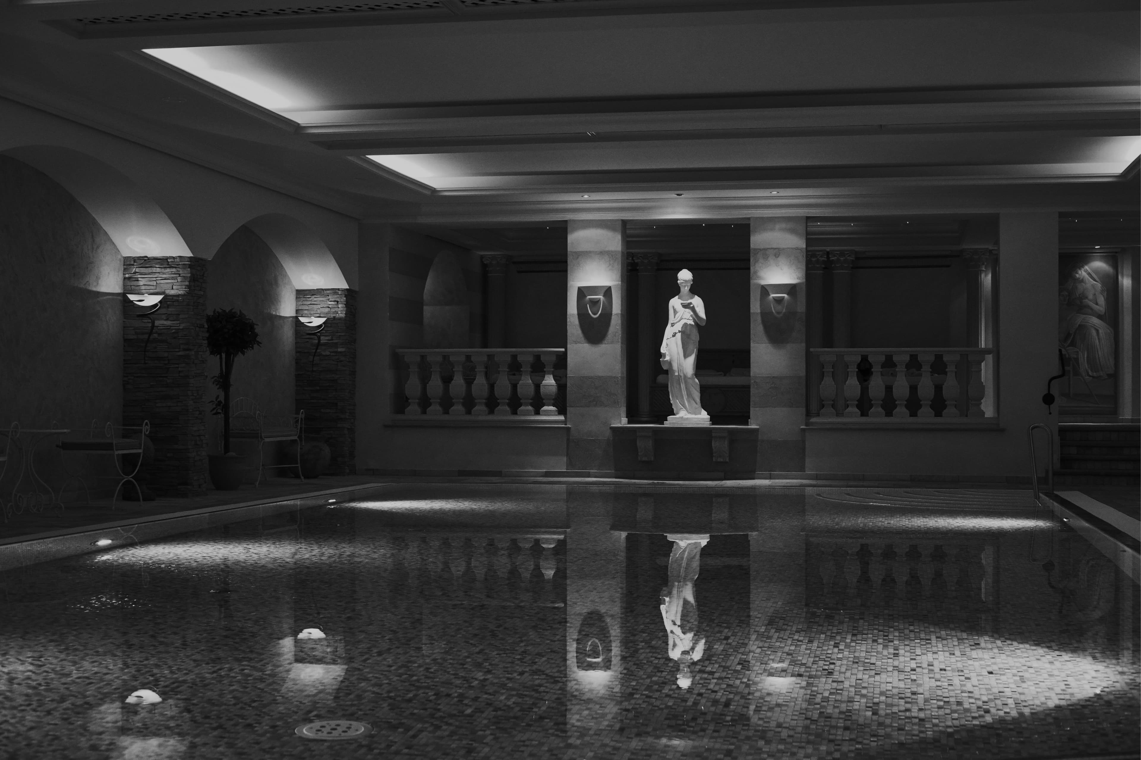 Hallenbad mit Säulen, Statue und spiegelglatter Wasserfläche, Schwarz-Weiß-Aufnahme
