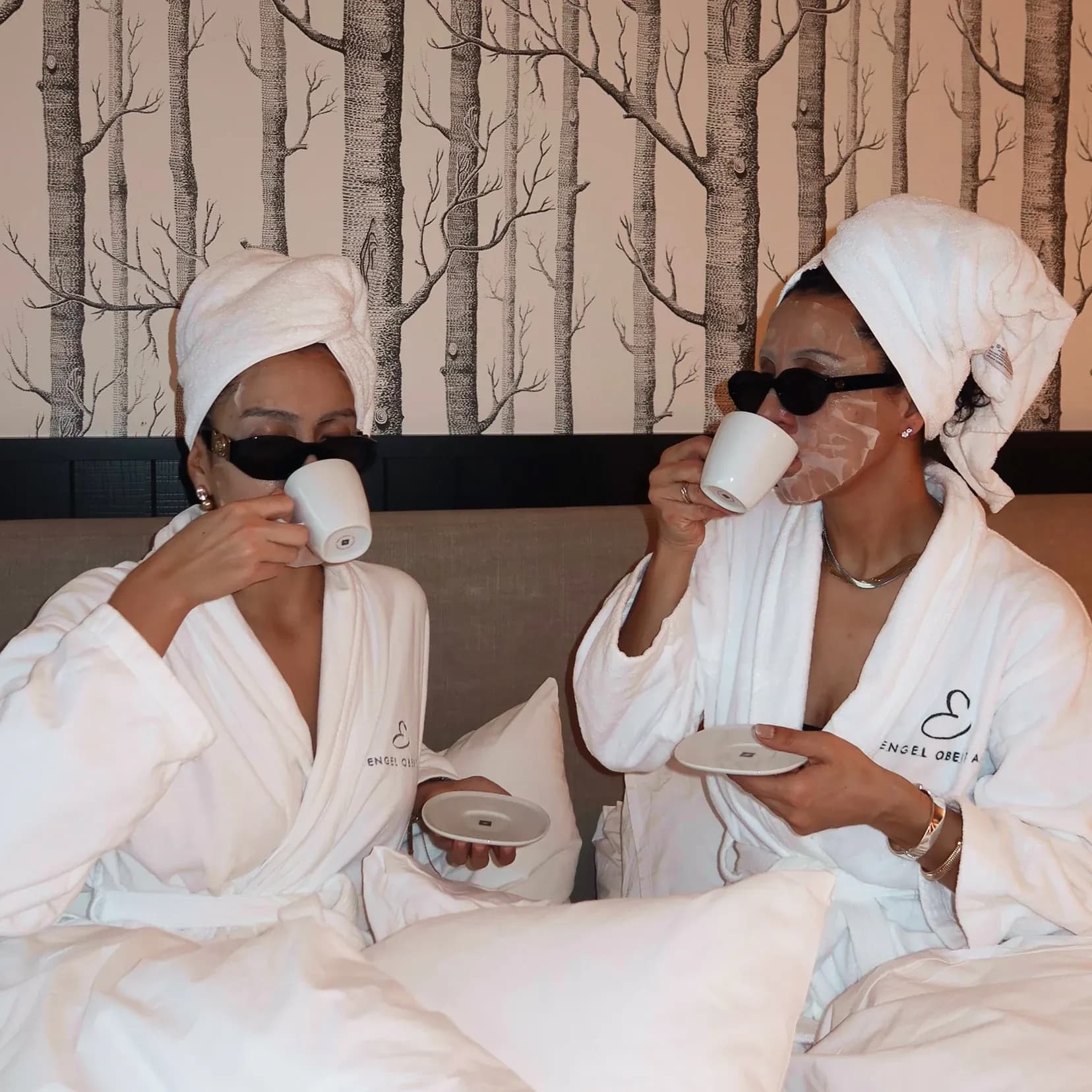 Zwei Frauen im Bademantel mit Handtuchturban trinken Kaffee im Bett