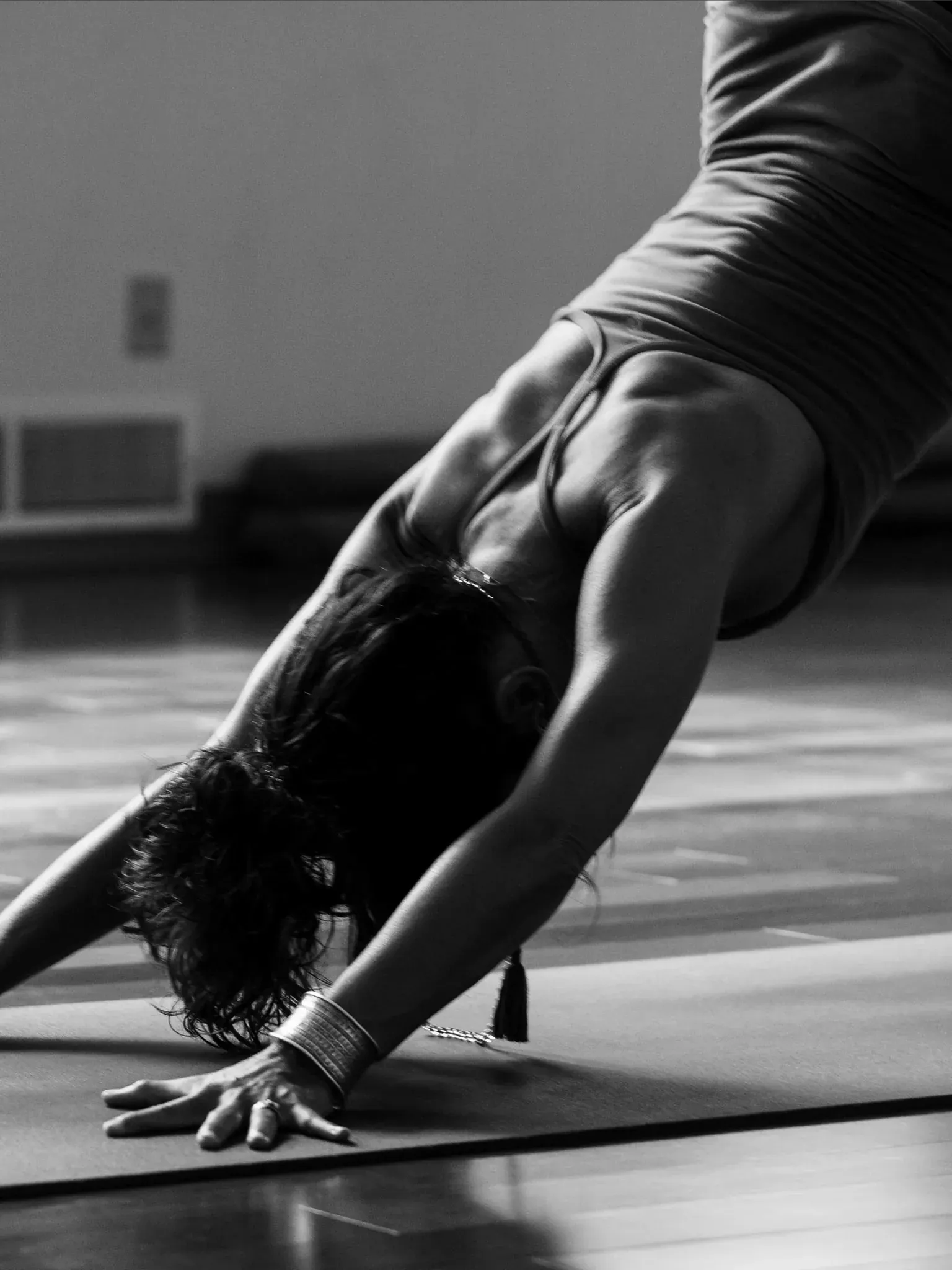 Schwarzweiß-Aufnahme einer Person in der Yoga-Haltung herabschauender Hund auf einer Matte.