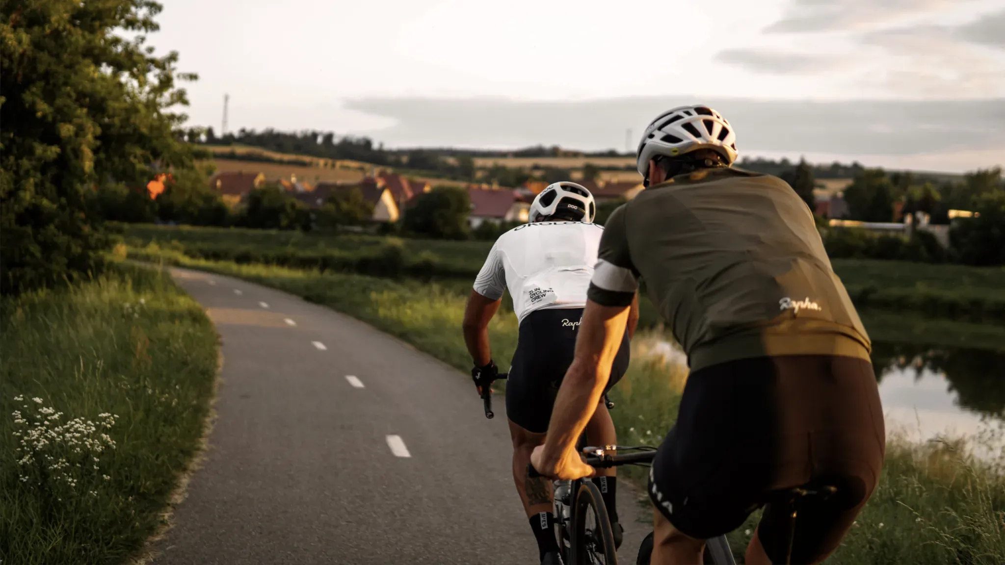 Zwei Rennradfahrer fahren nebeneinander auf einer Landstraße durch hügelige Wiesenlandschaft.