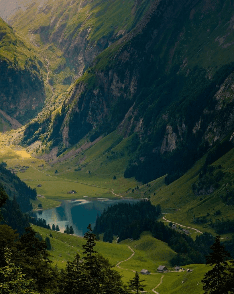 Alpines Tal mit türkisfarbenem Bergsee, umgeben von steilen grünen Hängen und verstreuten Chalets