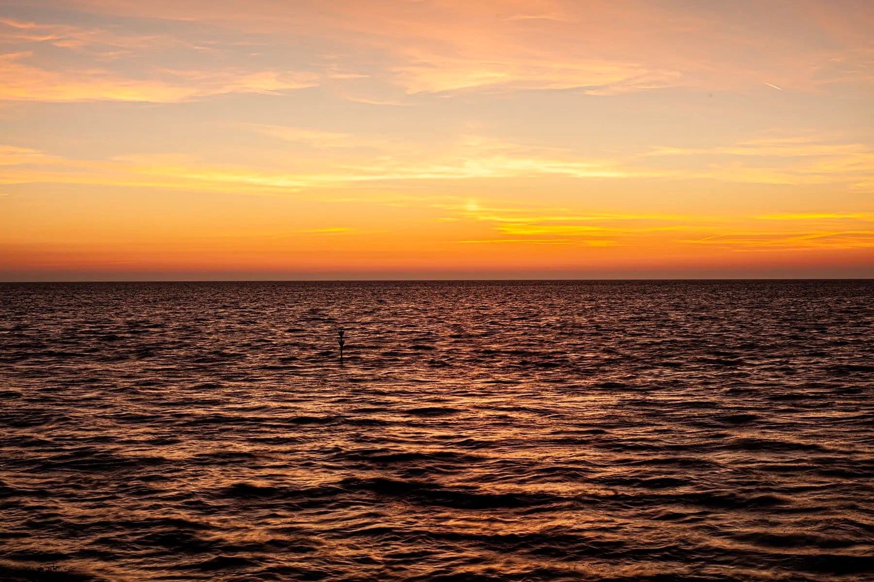Sonnenaufgang über der Nordsee mit tieforangenem Himmel, gespiegelt im ruhigen dunklen Wasser
