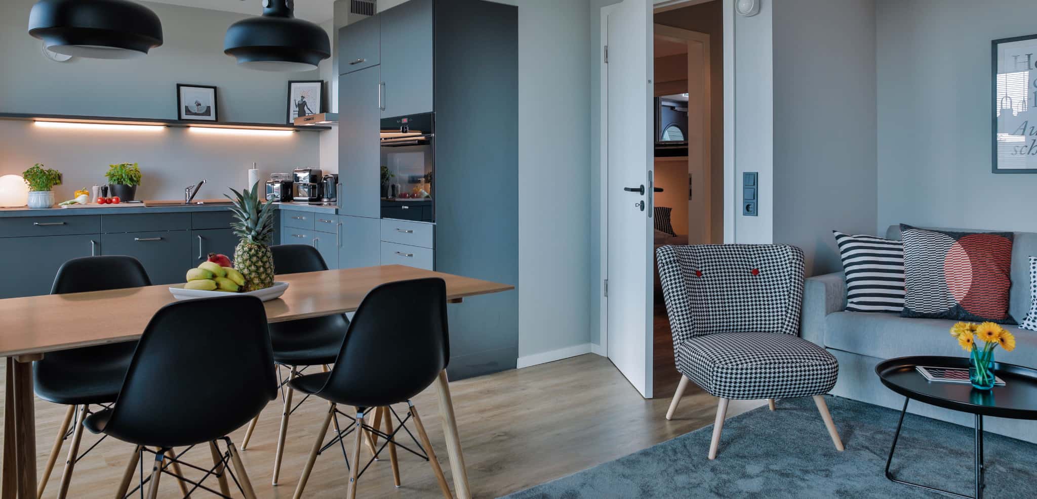 Wohnküche im Appartement mit Esstisch und schwarzen Stühlen, Küchenzeile, Sessel und Sofa