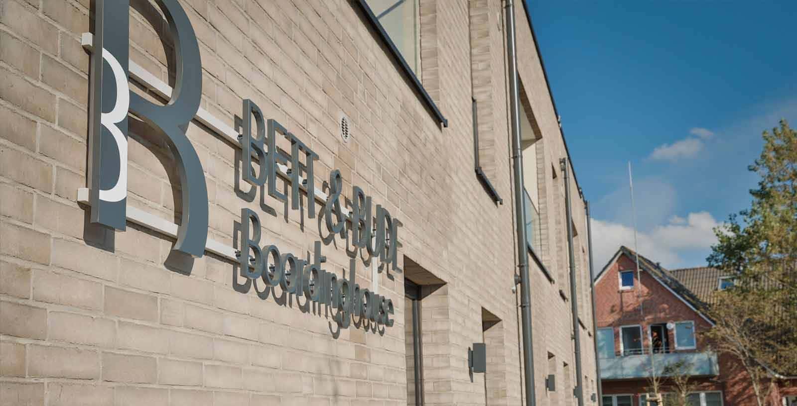 Fassade des Boardinghouse Bett & Bude aus hellem Backstein mit Schriftzug und Logo in Westerland