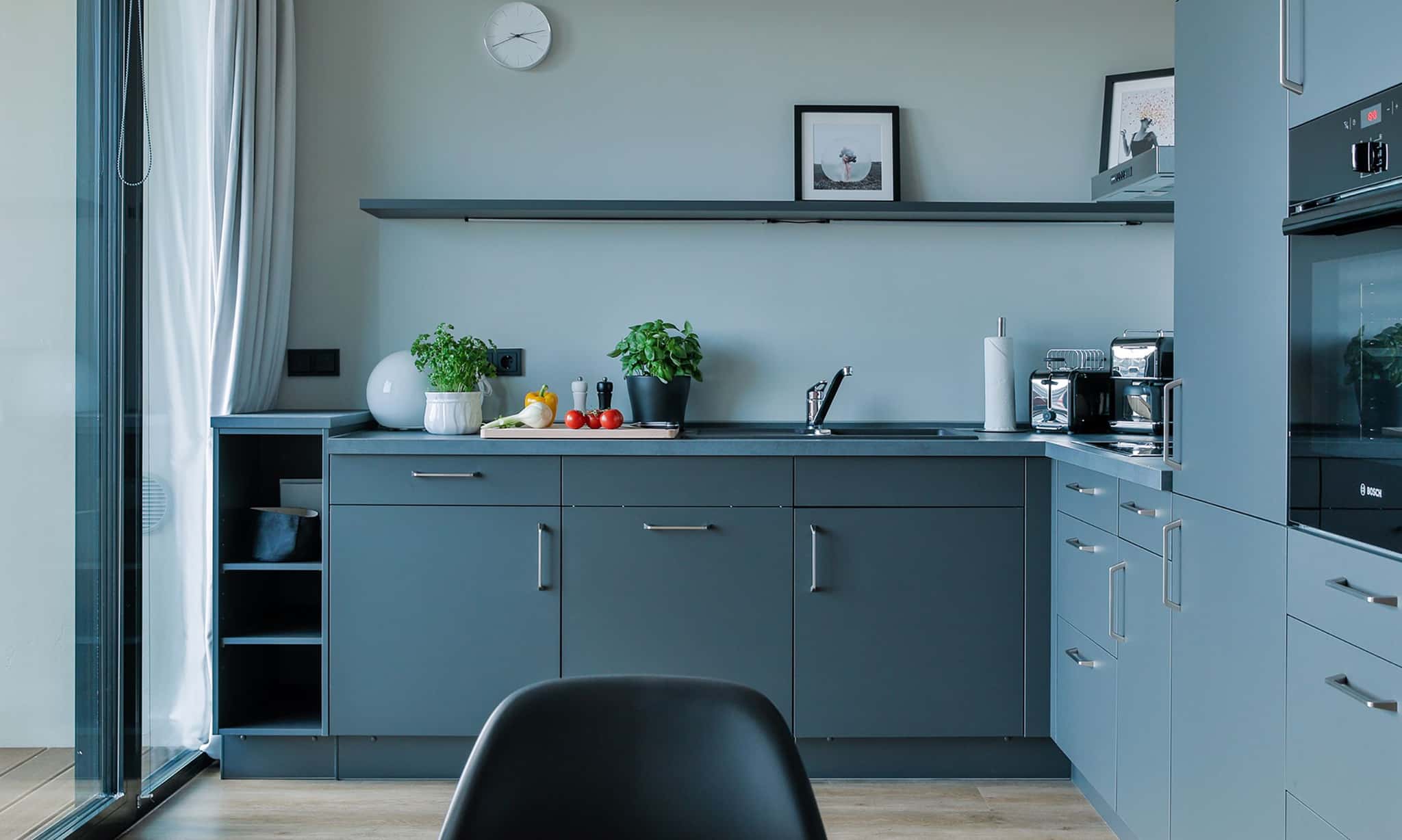 Küche mit grauen Fronten, Backofen, Kräutertöpfen und Wandboard im Appartement Bett & Bude