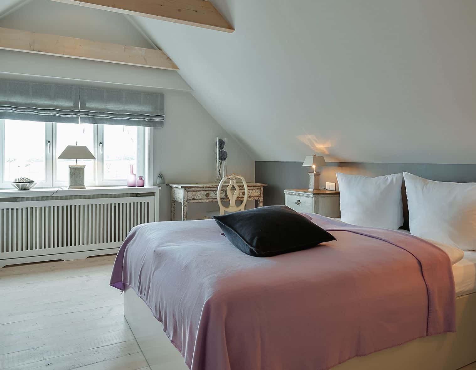 Schlafzimmer unter der Dachschräge mit Doppelbett, fliederfarbener Tagesdecke und antikem Schreibtisch im Fährhüs