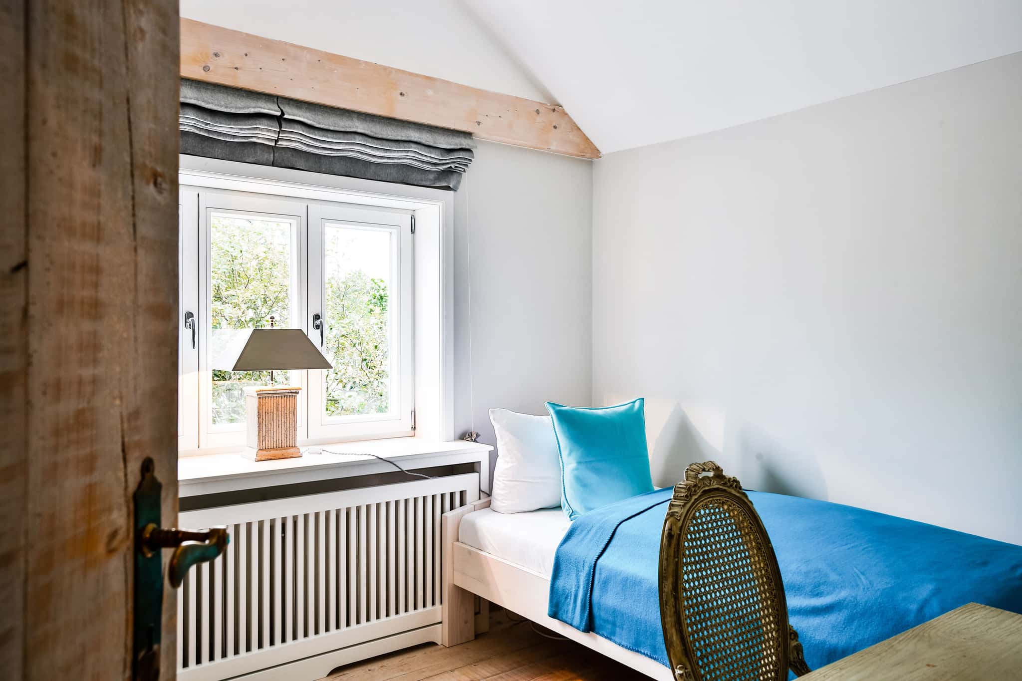 Schlafzimmer mit Einzelbett, türkisfarbener Decke und Fenster mit Blick ins Grüne im Fährhüs