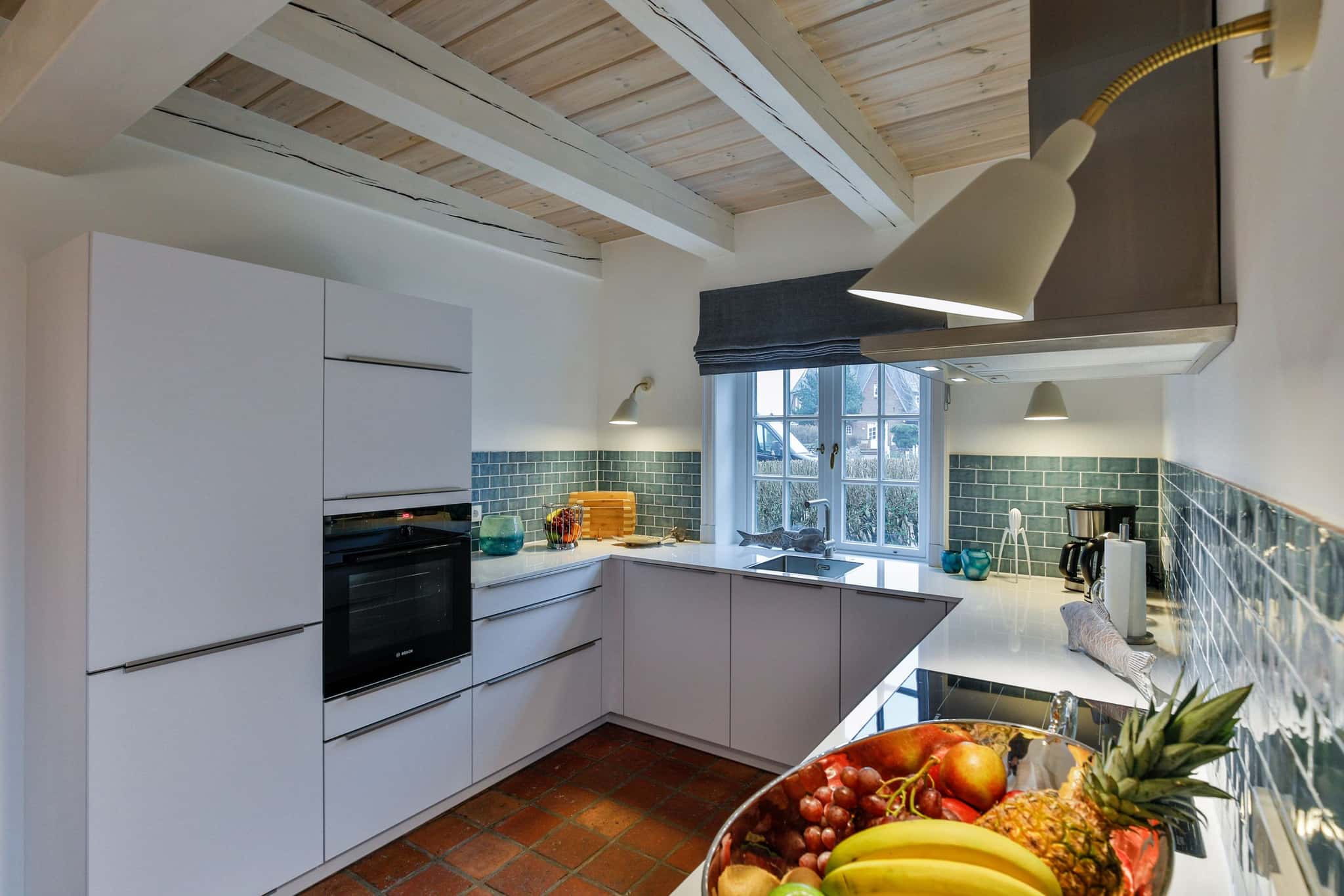 Küche mit weißen Fronten, blaugrünen Wandfliesen, Backofen und Sprossenfenster im Haus Lochterbarig