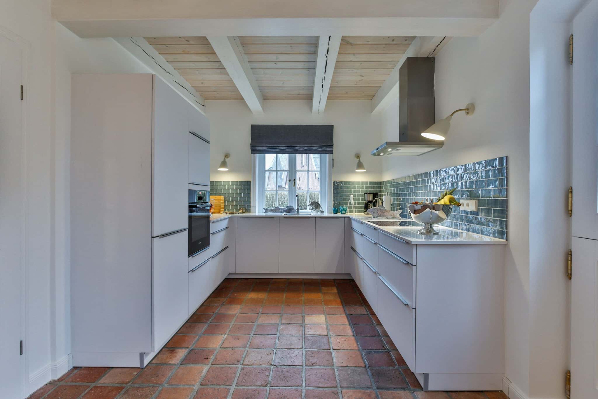 U-förmige Küche mit weißen Fronten, blaugrünen Wandfliesen und Terrakottaboden im Haus Lochterbarig