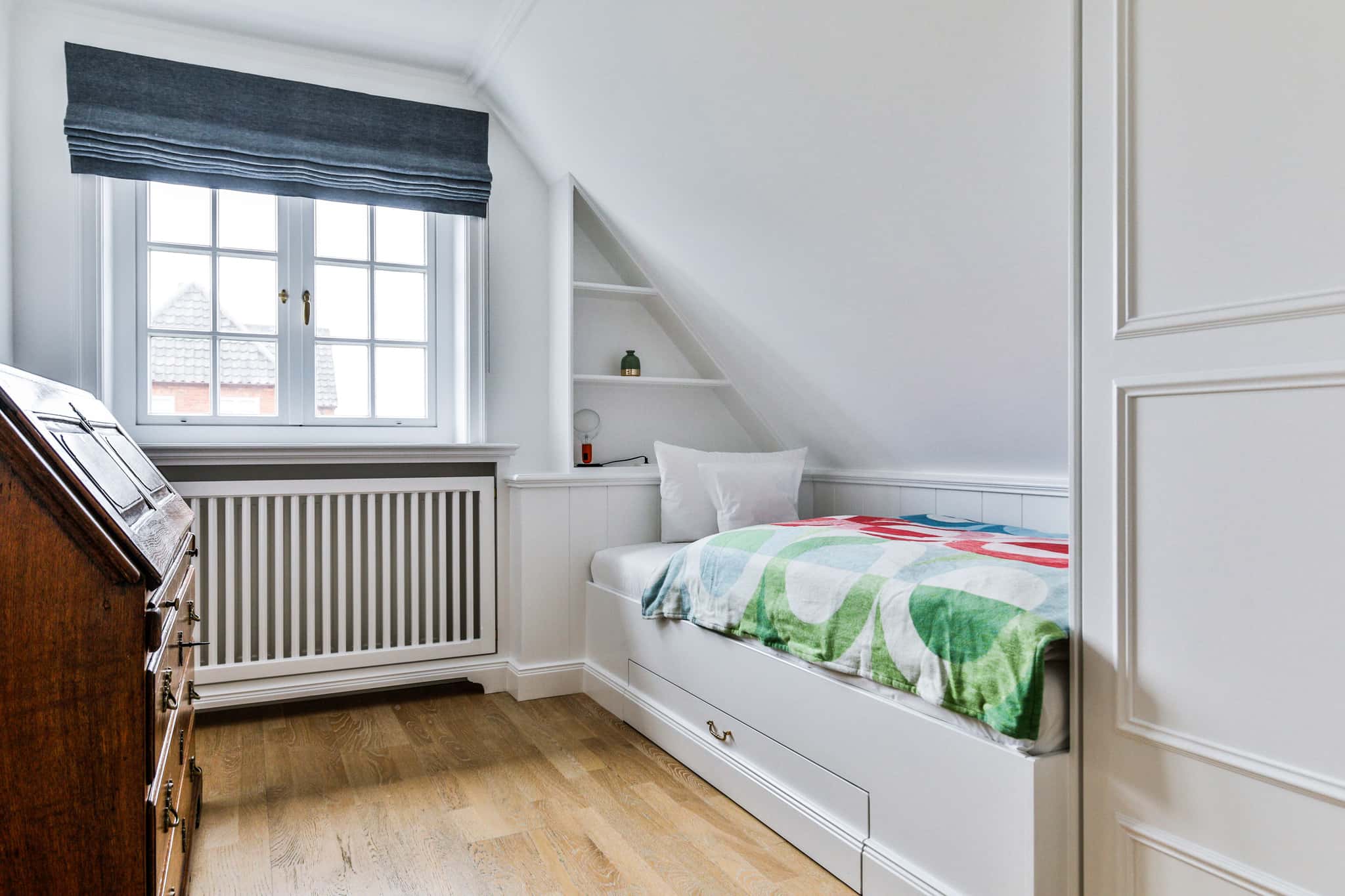 Schlafzimmer mit Einzelbett unter der Dachschräge, Einbauregal und antikem Sekretär im Haus Lochterbarig