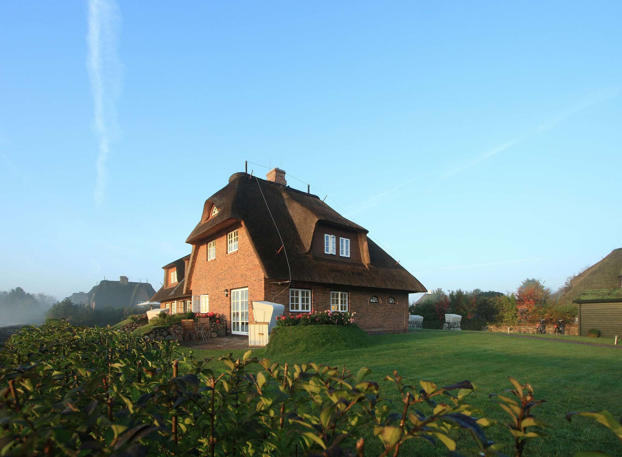 Reetgedecktes Friesenhaus Lüüvhoog aus rotem Backstein mit Garten und Strandkörben am Morgen